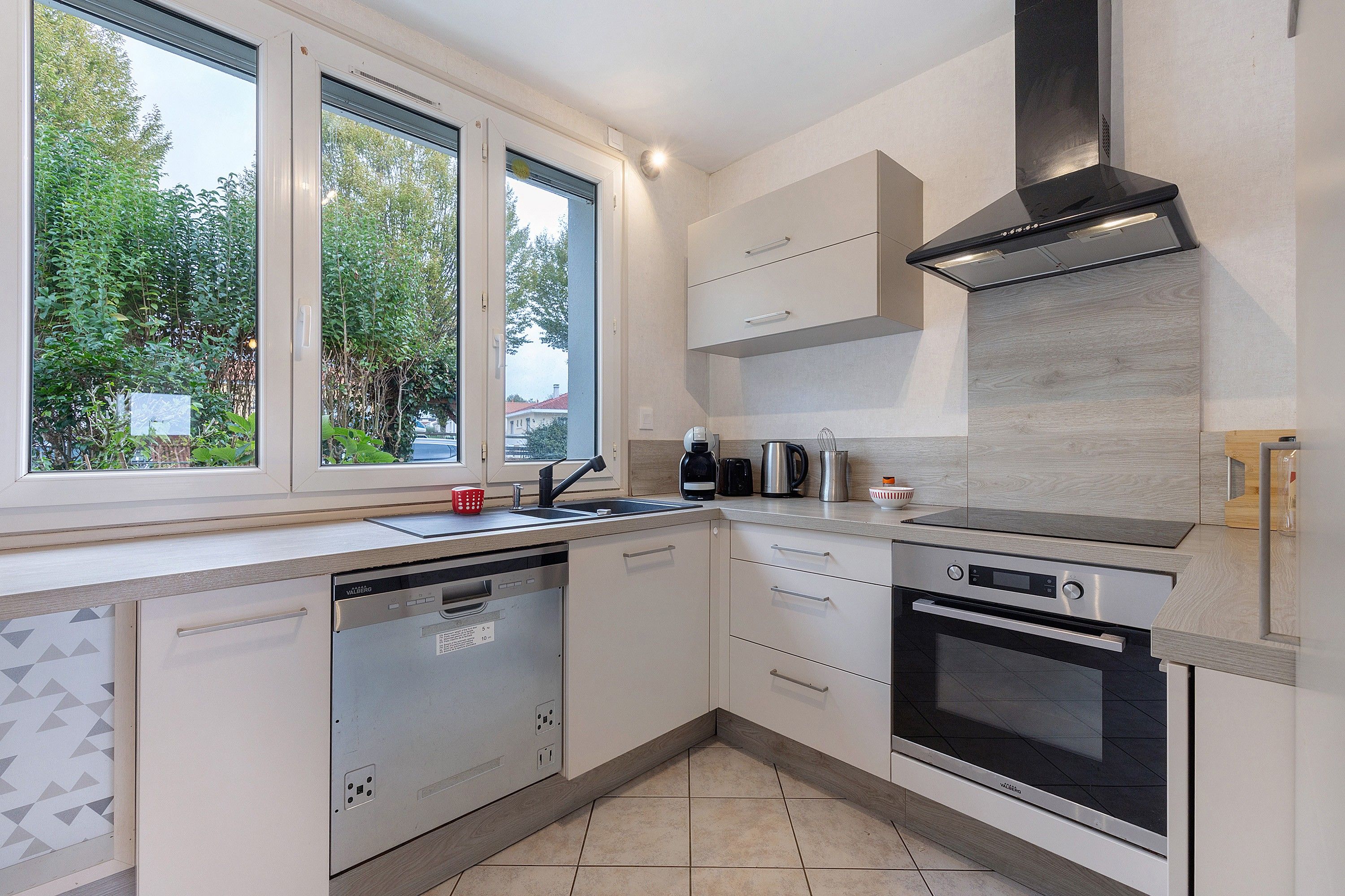 Een moderne keuken met een vaatwasser, oven en een raam met uitzicht op groen.