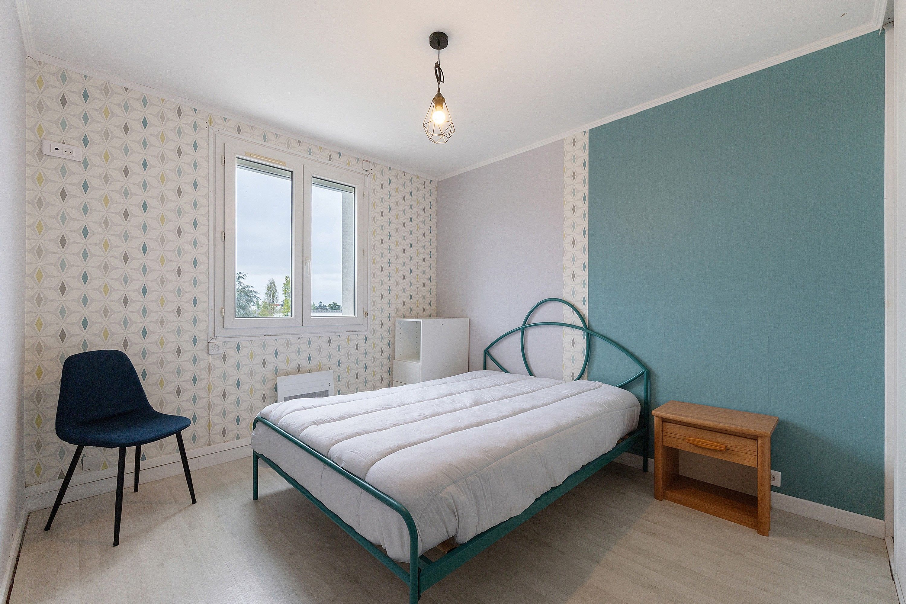 Une chambre à coucher avec un lit, une chaise, une table de chevet et une fenêtre.