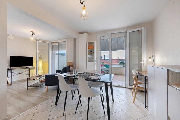 Un espace de repas moderne avec une table dressée pour quatre personnes, un téléviseur et une vue sur l’extérieur.