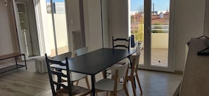 Un espace repas comprenant une table et des chaises, un banc, et une vue sur l’extérieur par une porte vitrée.