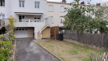 Edifício residencial com entrada frontal, escadaria que dá para uma varanda e um quintal cercado.