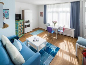Ein Wohnzimmer mit einer Couch, einem Couchtisch, einem Esstisch mit Stühlen, einem Schrank und einer Heizung.