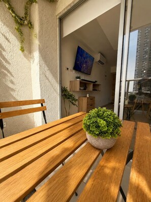 A wooden bench with a potted plant, a television mounted on the wall, and a view of a building through a glass door. - Coral Bay | Pool, Wifi & Beach (Cartagena)