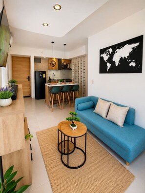 A modern apartment with a blue sofa, a small round table with a bonsai, a kitchen with a dining area, and a world map on the wall. - Coral Bay | Pool, Wifi & Beach (Cartagena)