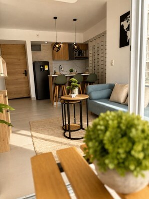 A modern kitchen with a refrigerator, wooden cabinets, and a dining area with chairs and a table. - Coral Bay | Pool, Wifi & Beach (Cartagena)