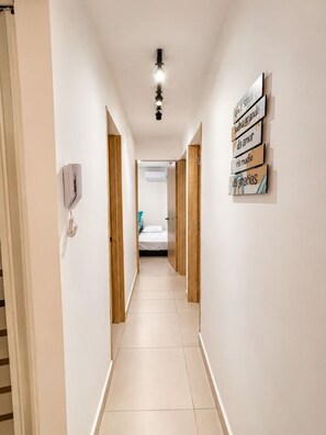 A narrow hallway with a bed at the end, a wall-mounted light fixture, and a sign with text. - Coral Bay | Pool, Wifi & Beach (Cartagena)
