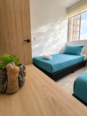 A bedroom with a bed, a bedside table with a plant, and a window with a view of buildings. - Coral Bay | Pool, Wifi & Beach (Cartagena)