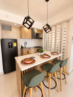 A modern kitchen with a central island, bar stools, a refrigerator, and pendant lighting. - Coral Bay | Pool, Wifi & Beach (Cartagena)