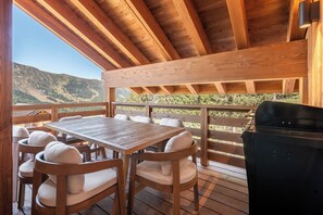 Eine Terrasse aus Holz mit Tisch, Stühlen, einem Grill und Blick auf eine Berglandschaft.
