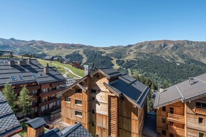 Eine Holzchalet mit mehreren Balkonen, dahinter ein Skipisten und eine gebirgige Landschaft.
