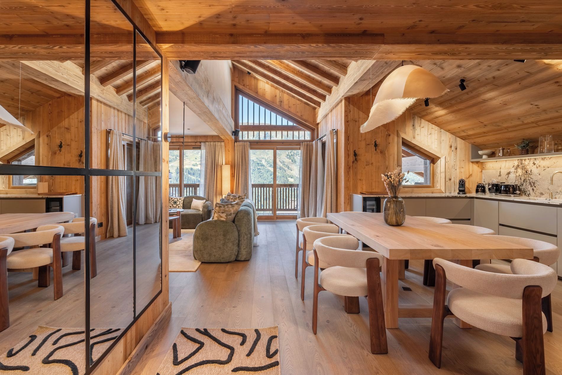 A spacious wooden interior with a dining area, kitchen, and a view through a large window.