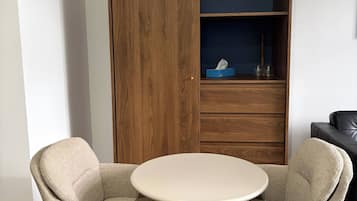 A room with a round table and two chairs, a wooden wardrobe, and a dark-colored sofa.