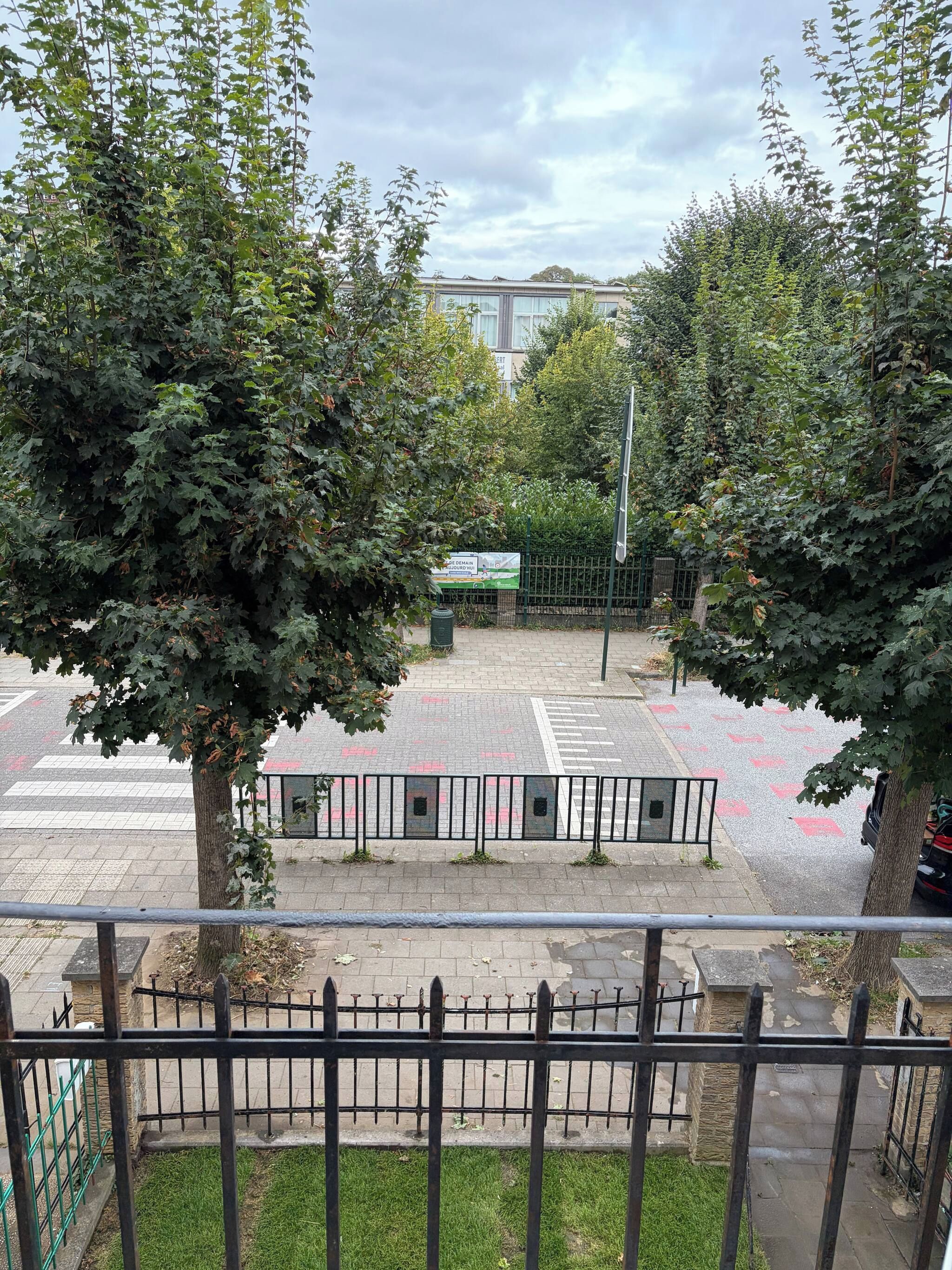Une vue d’une zone de stationnement avec un panneau vert, un passage piéton et une clôture métallique.