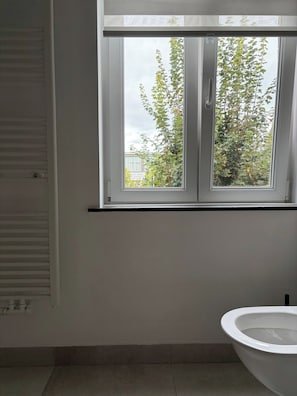 Ein Badezimmer mit Toilette, einem Fenster mit Blick auf Bäume und ein Gebäude sowie einer Heizung.