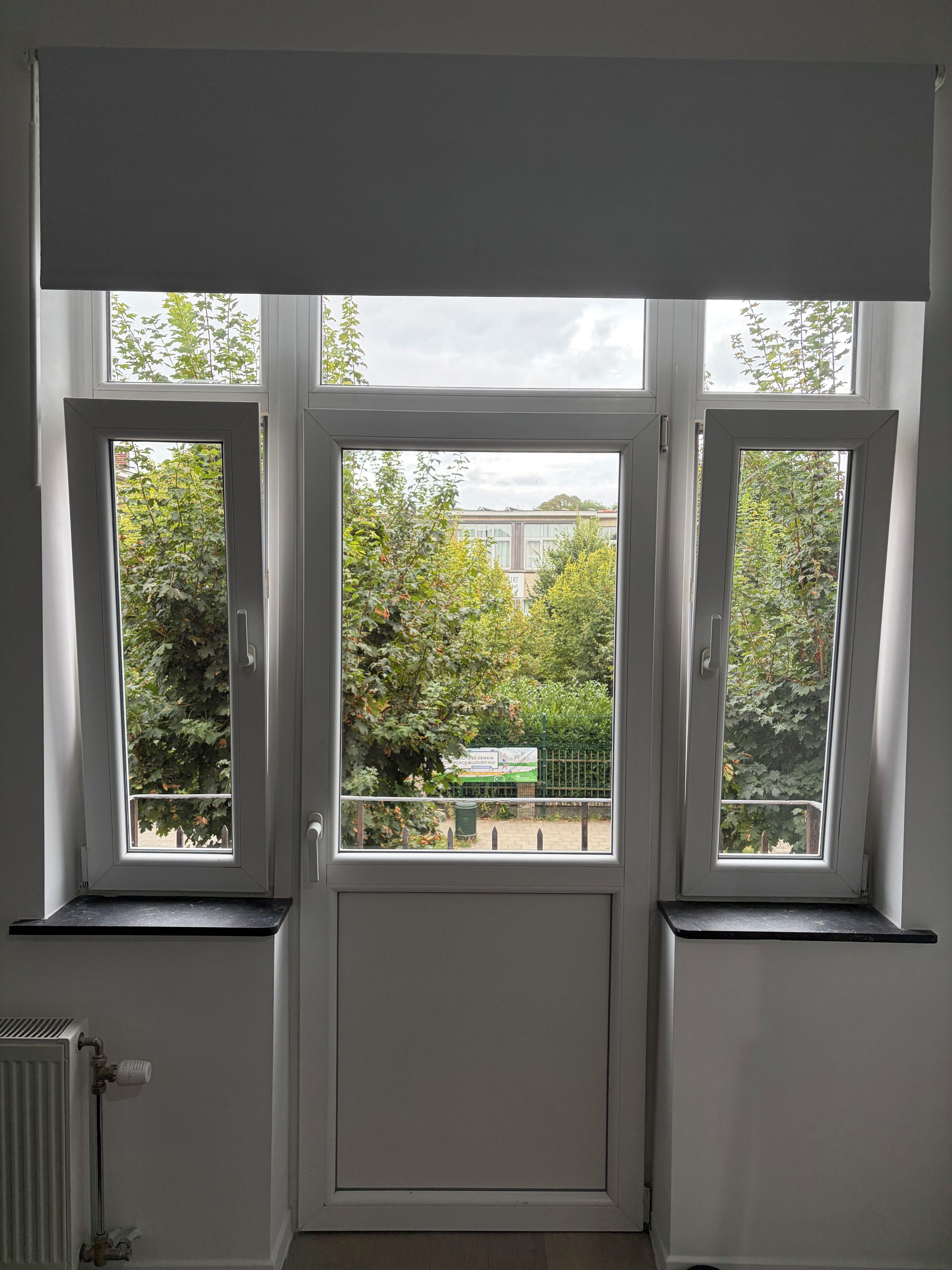 Une pièce avec une grande fenêtre, un radiateur et une porte.