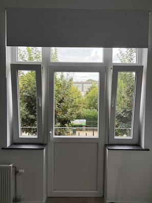 Een kamer met een groot raam, een radiator en een deur.