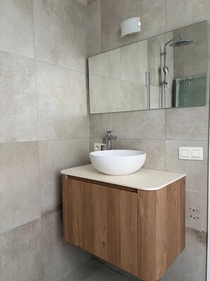 A modern bathroom with a large mirror, a vessel sink, and a shower.