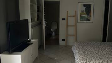 Een kamer met een bed, een televisie op een kast, een badkamer met toilet en een schilderij aan de muur.