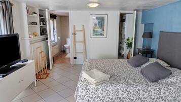 Quarto com cama, televisão, guarda-roupa, banheiro e um quadro na parede.