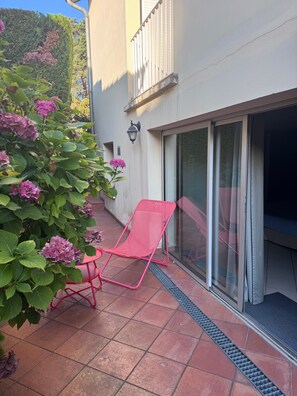 Eine Terrasse mit einem roten Stuhl, einem Blumentopf mit rosa Blüten und einer Schiebetür.