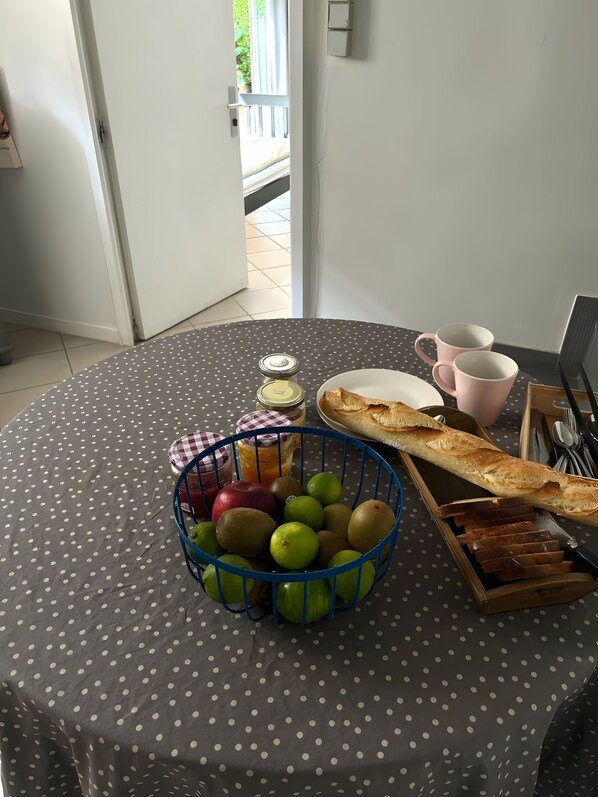 A table with a polka dot tablecloth, a basket of fruits, a loaf of bread, and a jar of jam.