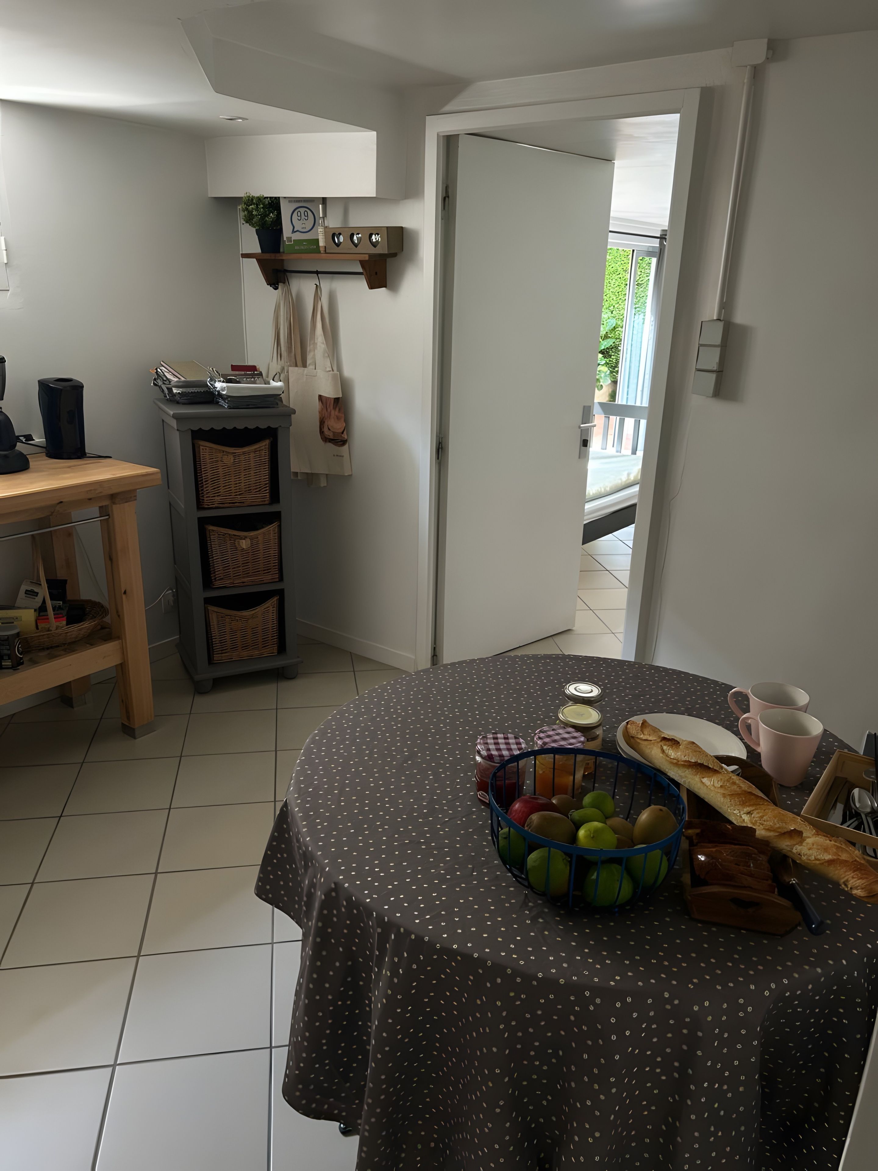 Eine Küche mit einem runden Tisch, der mit einer Tischdecke mit Punkten bedeckt ist, einer Obstkorb und einem Baguette.