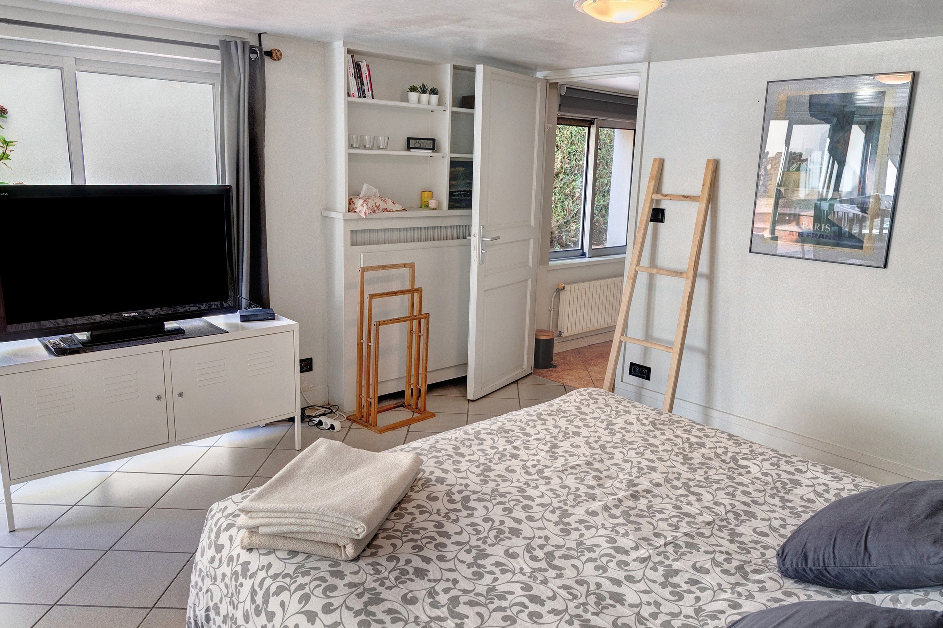 Une chambre à coucher avec un lit, un téléviseur posé sur un meuble, une échelle et une fenêtre donnant sur un paysage verdoyant.