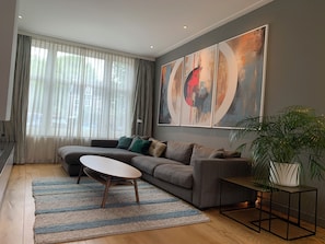 Ein modernes Wohnzimmer mit einer Eckcouch, einem Couchtisch, einer Topfpflanze und abstrakter Wandkunst.