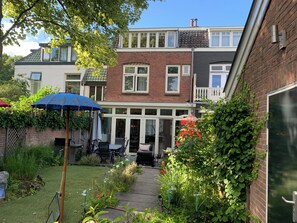 Ein Garten mit Wohnbereich, einer Terrasse, Sitzgelegenheiten im Freien und verschiedenen Pflanzen.