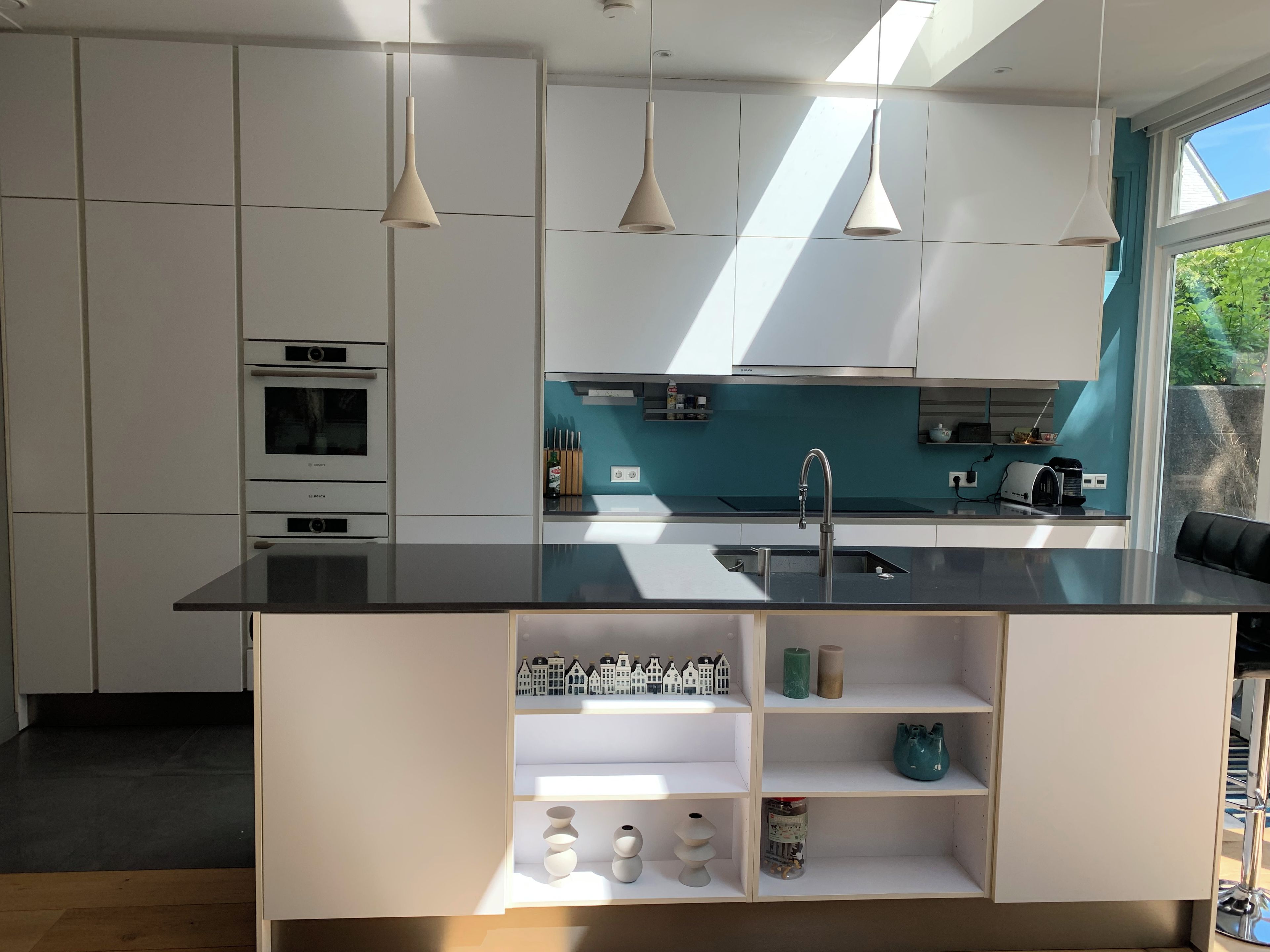 Una cocina moderna con armarios blancos, encimera negra e iluminación colgante.