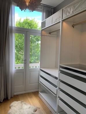 A room with a white wardrobe, a fur rug, and a view of greenery outside.