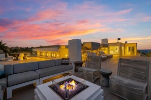 Eine Dachterrasse mit Feuerstelle, Sitzgelegenheiten im Freien und Blick auf den Sonnenuntergang.