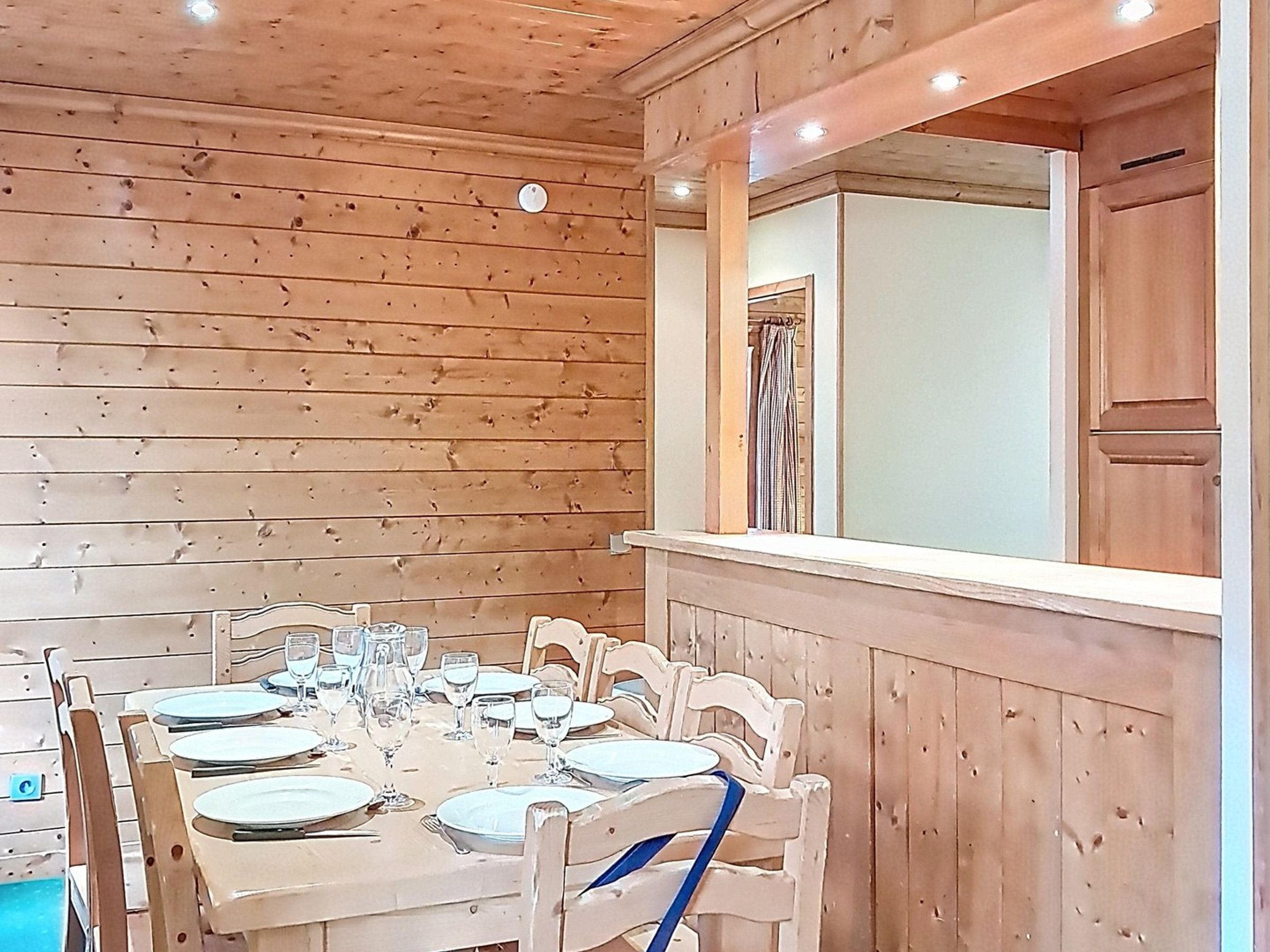 A wooden interior with a dining table set for four, chairs, a window with a view, and a wooden cabinet.