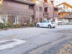 Een witte auto geparkeerd op een straat voor een gebouw met houten balkons en een bord waarop staat 'MOUNTAIN collection'.