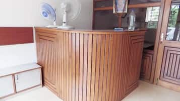 Ein Empfangsschalter mit Holzoptik, zwei Standventilatoren und ein gerahmtes Bild an der Wand.