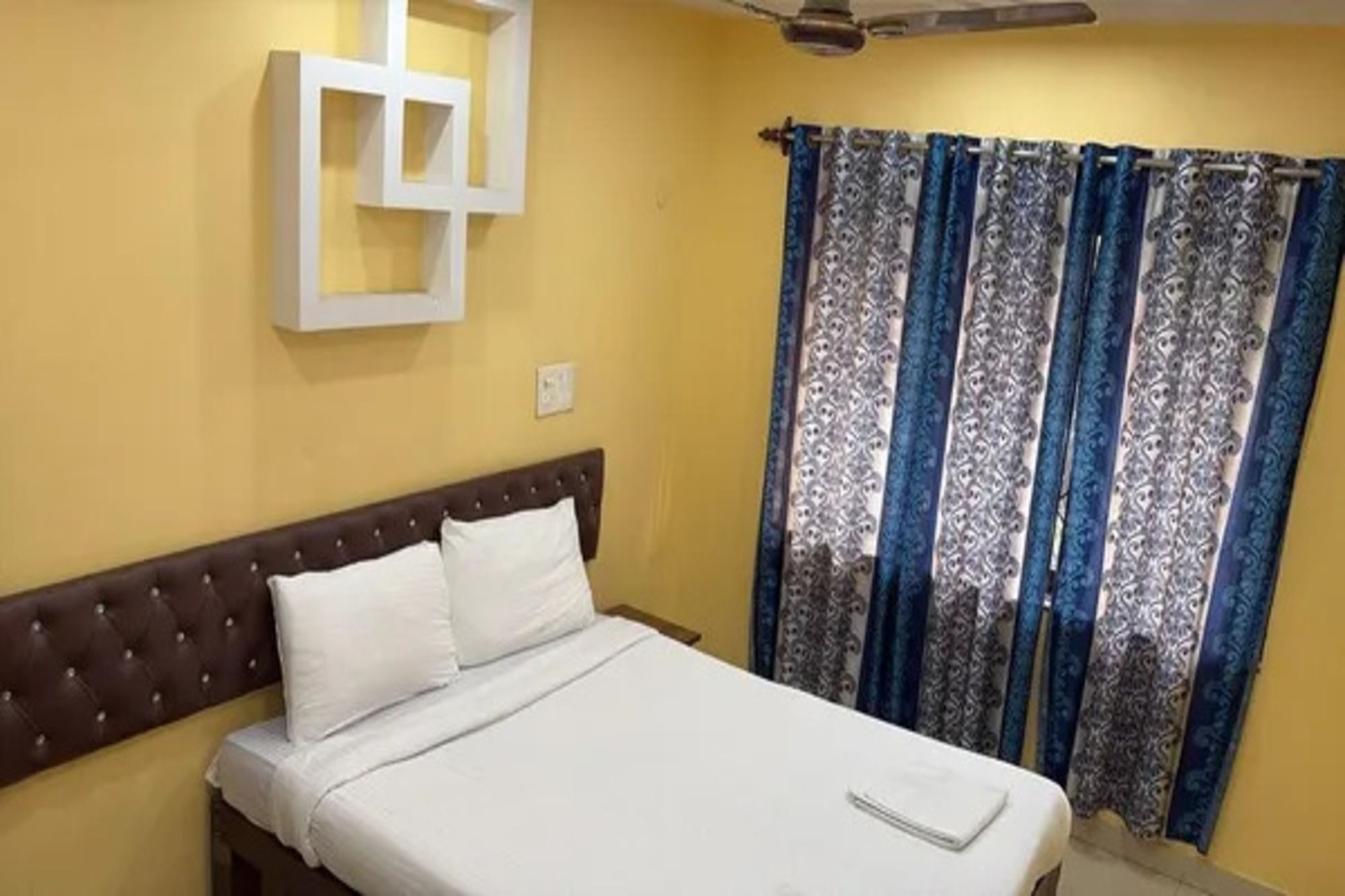 Un dormitorio con una cama, un ventilador de techo y una ventana con cortinas estampadas.