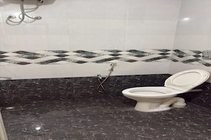 A bathroom with a toilet, a shower, and a tiled wall with a geometric pattern.