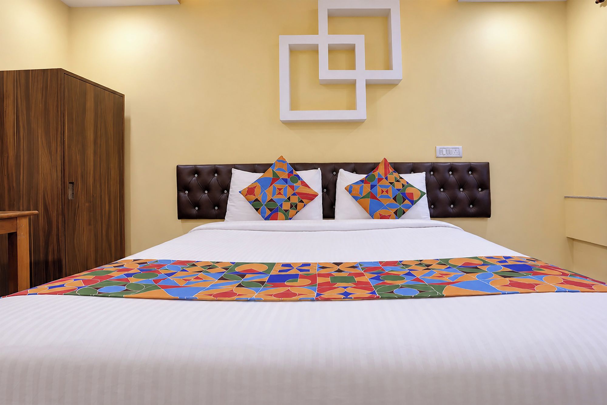 A hotel room with a bed, a wooden wardrobe, and a wall-mounted light fixture.