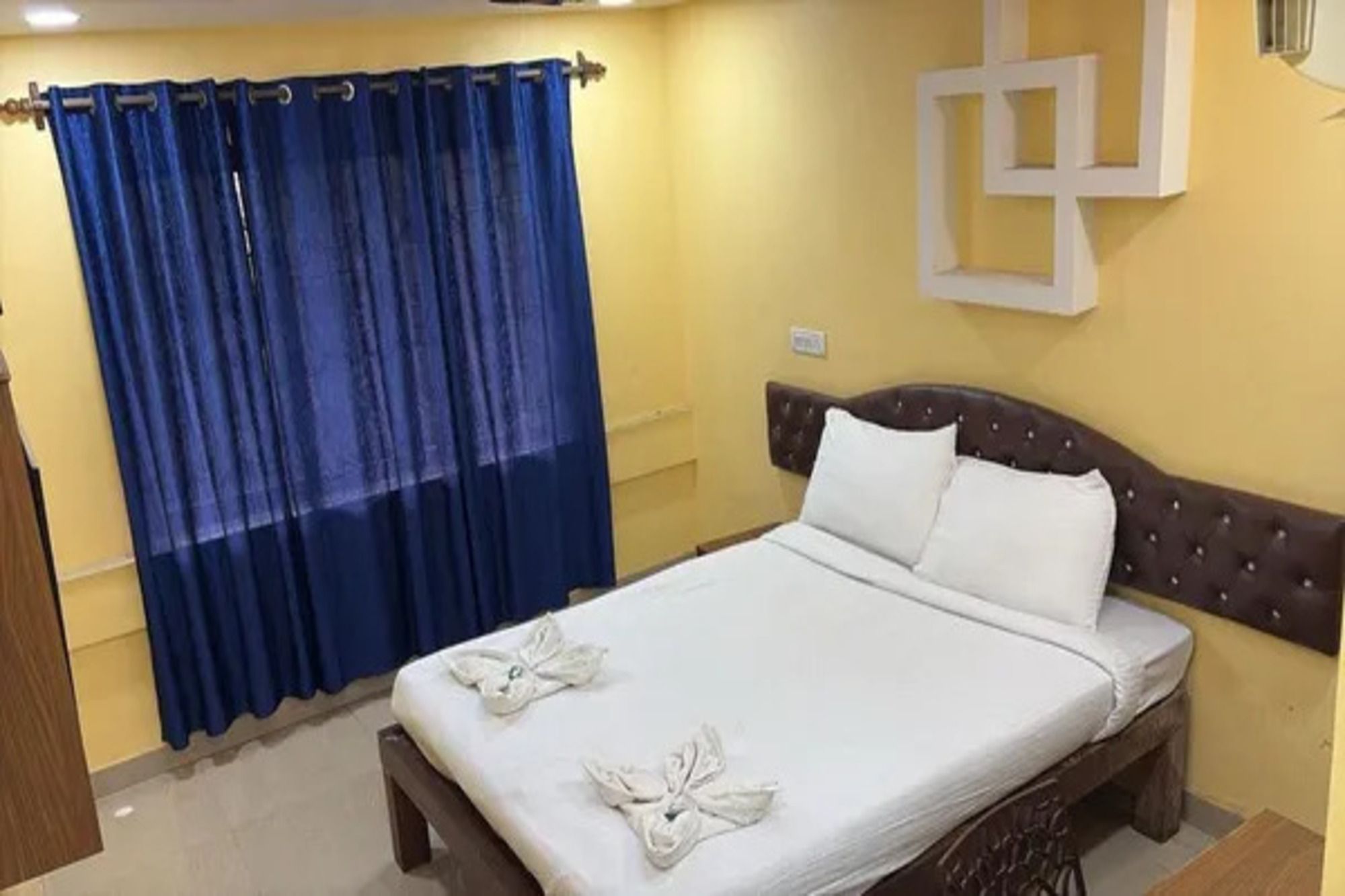 Una habitación de hotel con cama, cortinas y una lámpara fijada a la pared.