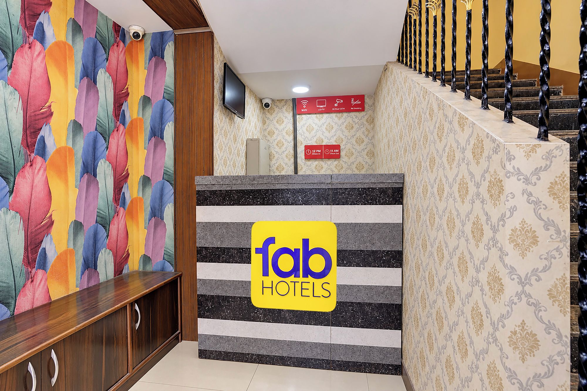 A hotel reception area with a colorful abstract wall, a sign for 'fab hotels', and a staircase with a patterned railing.