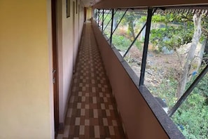 A corridor with a checkered floor, a window with a metal frame, and a view of greenery outside.