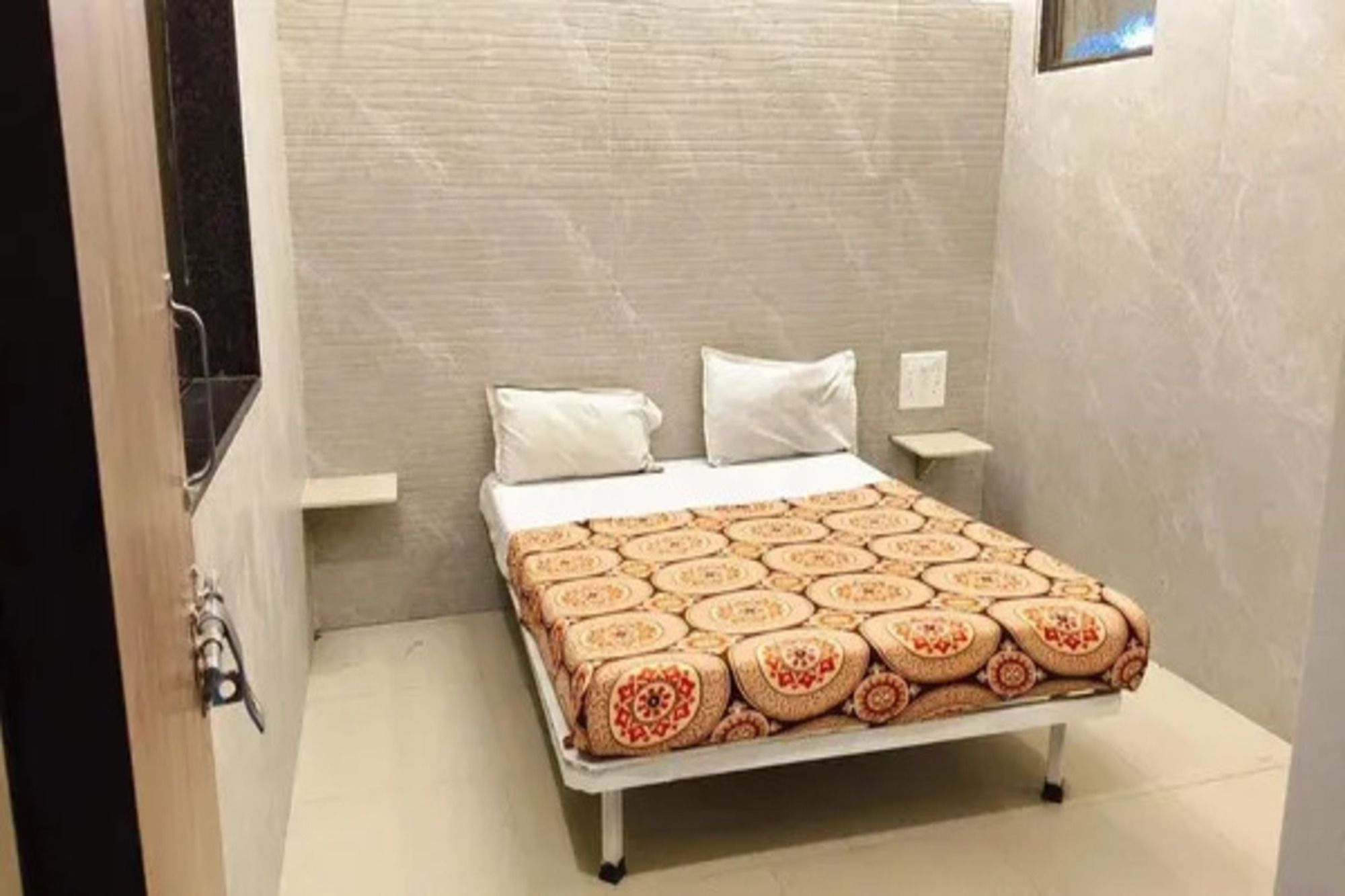 Pequeña habitación con cama individual, colcha estampada, mesita de noche y luz de pared.