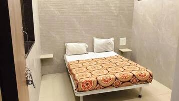 Pequeña habitación con cama individual, colcha estampada, mesita de noche y luz de pared.