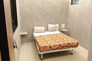 Pequeña habitación con cama individual, colcha estampada, mesita de noche y luz de pared.
