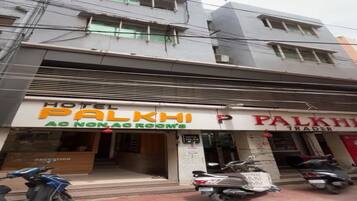 Hotel Palkhi, con un cartel que indica 'Habitación con aire acondicionado/sin aire acondicionado' y una sección 'Trader'. Hay scooters estacionados al frente.