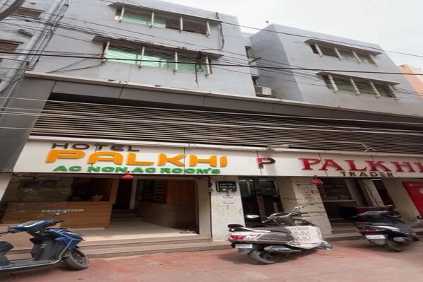 Hotel Palkhi, con un cartel que indica 'Habitación con aire acondicionado/sin aire acondicionado' y una sección 'Trader'. Hay scooters estacionados al frente.