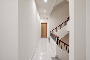 Un intérieur moderne avec un couloir menant à une porte en bois, un escalier doté d’une rampe en bois et un sol carrelé.