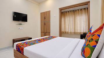 A hotel room with a bed, a television mounted on the wall, a wardrobe, and a window with curtains.