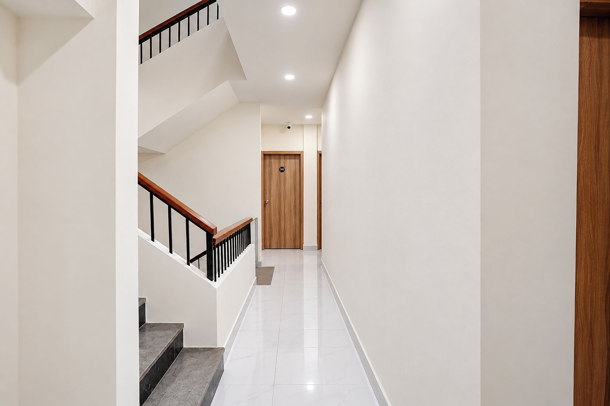 Un interior moderno con una escalera, una puerta de madera y un suelo blanco e impecable.