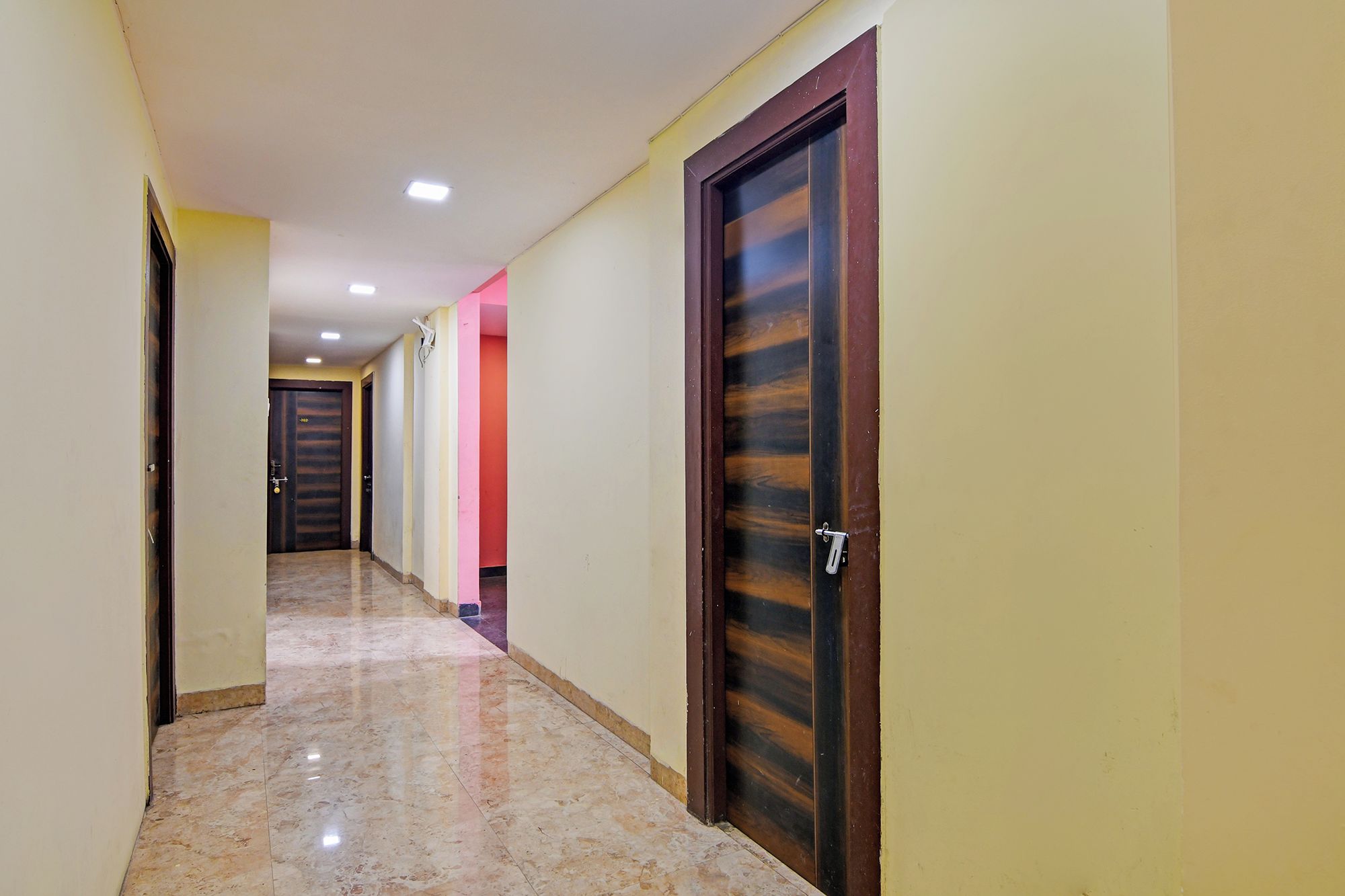 Un pasillo con puertas, piso de baldosas e iluminación empotrada en el techo.